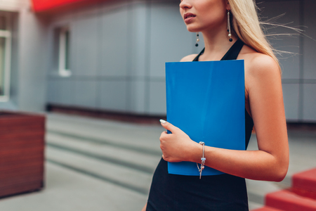 Young blonde businesswoman holding folder waiting for meeting by business center in city. Business, communication, technology and people conceptの写真素材