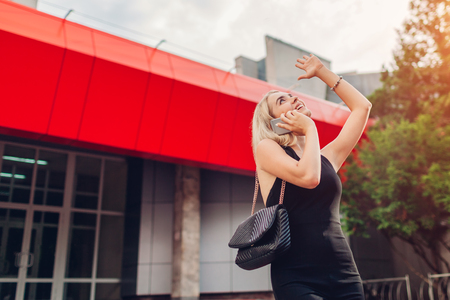 Happy blonde businesswoman talking on smartphone and reacts to great news by modern business center. Success. Excited woman raised hands.の写真素材