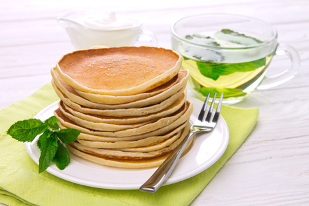 Stack of pancakes with mint, tea and sour cream on white wooden backgroundの写真素材