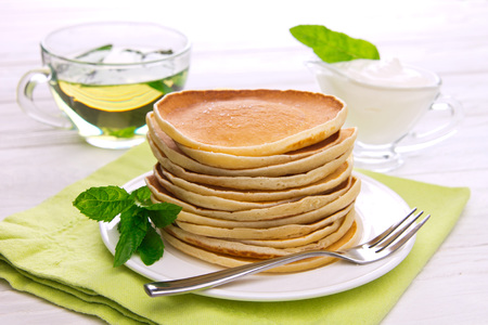 Stack of pancakes with mint, tea and sour cream on white wooden backgroundの写真素材