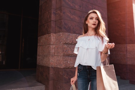Beautiful stylish young woman with shopping bags walking out of shopping center. Sale. Summer fashionの写真素材