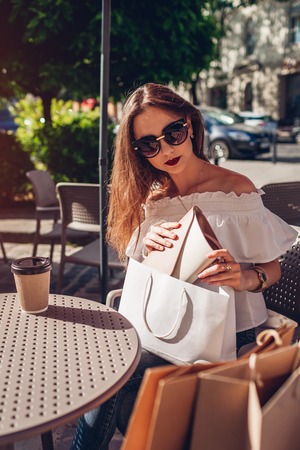 Beautiful stylish young woman with shopping bags chilling in outdoor cafe on city street and checking her purchases.の写真素材