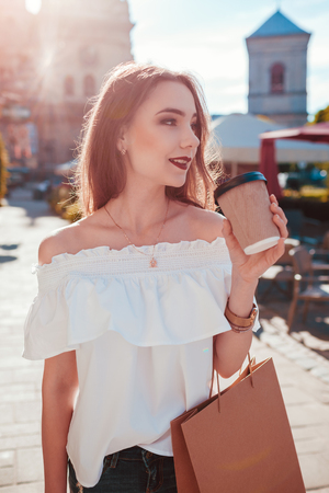 Beautiful stylish young woman with shopping bags chilling on city street and drinking coffee. Summer fashionの写真素材