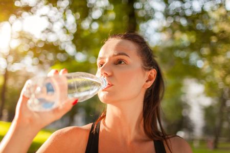 Young sportive woman drinking water after workout in summer park. Healthy way of lifeの写真素材