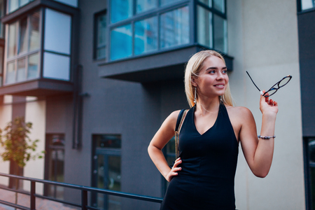 Happy blonde businesswoman wearing glasses by business center in city. Fashion model. Formal style clothing and accessoriesの写真素材
