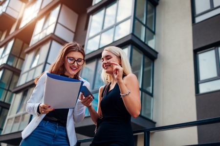 Real estate agent presenting new apartment to client. Businesswoman shows contract to customer. Partners laughing while checking documentsの写真素材