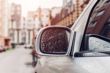 Side rear-view mirror on a modern car on city street background. Rainy water drops on glass.の写真素材