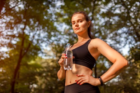 Young sportive woman drinking water after workout in summer park. Healthy way of life. Active lifestyleの写真素材