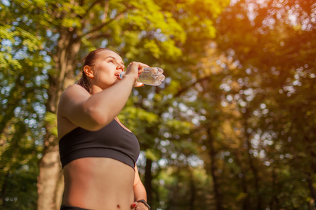 Young sportive woman drinking water after workout in summer park. Healthy way of life. Active lifestyle. Importance of waterの写真素材