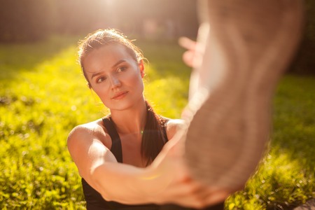 Young sportive woman doing exercises in summer park. Sportswoman stretching her legs sitting on grass. Sport conceptの写真素材