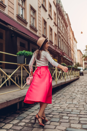 Young woman wearing stylish clothing, jewellery and accessories outdoors. Model walking on old city street in hat by cafe. Beauty fashion conceptの写真素材