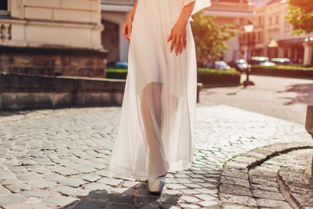 Beautiful woman wearing white wedding dress outdoors in summer. Lady walking by palace at sunsetの写真素材
