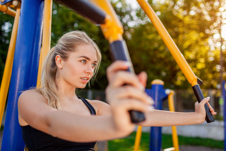 Young woman training on machine on sportsground in summer. Working on biceps musclesの写真素材