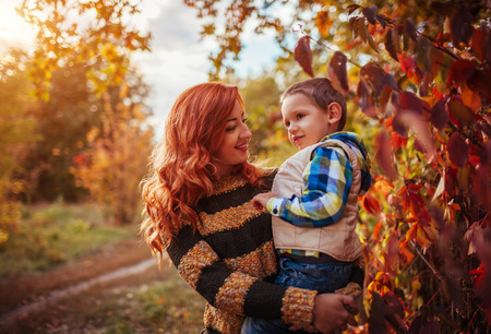 Happy mother and her little son walking and having fun in autumn forest. Kid is smilingの写真素材
