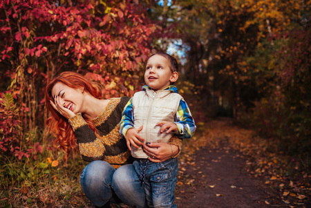 Happy mother and her little son walking and having fun in autumn forest. Kid and mom are laughingの写真素材