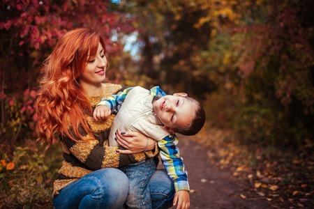 Happy mother and her little son walking and having fun in autumn forest. Kid is playingの写真素材