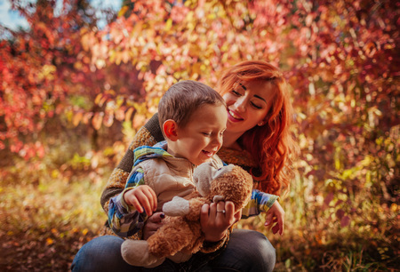 Happy mother and her little son walking and having fun in autumn forest. Kid is playing with a toyの写真素材