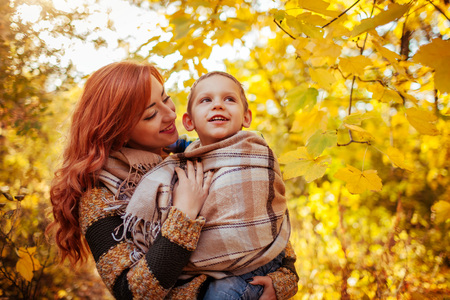 Happy mother and her little son walking and having fun in autumn forest. Woman wraps her kid in a scarfの写真素材