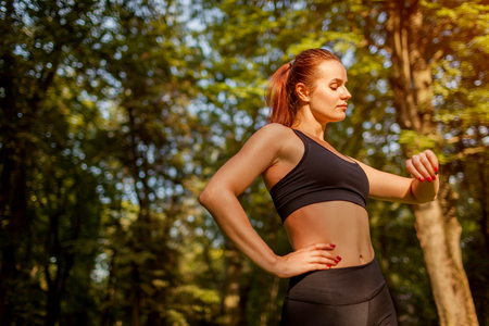 Runner checking burned calories on sports watch. Woman looking at watch in summer park at sunset. Sport conceptの写真素材
