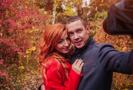 Young couple in love taking selfie using camera in autumn forestの写真素材