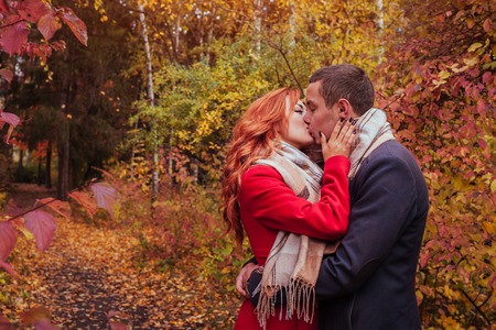 Young couple kisses in autumn forest among colorful treesの写真素材