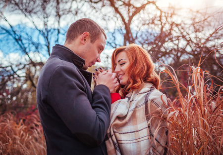 Young man warms his girlfriend's hands in autumn forest among high grassの写真素材