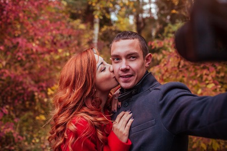Young couple in love taking selfie using camera in autumn forestの写真素材