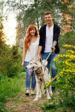 A young couple walking a husky dog in the spring parkの写真素材