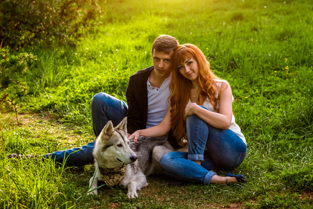 A young couple walking a dog in the spring park. People sitting on grass with huskyの写真素材