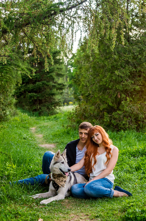 A young couple walking a dog in the spring park. People sitting on grass with huskyの写真素材