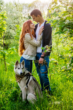 A young couple walking a dog in the spring park and kissing. Huskyの写真素材