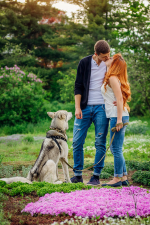 A young couple walking a dog in the spring park and kissing. Huskyの写真素材