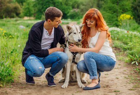 A young couple walking a dog in the spring park. Man and woman hugging huskyの写真素材