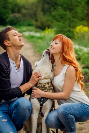 A young couple walking a dog in the spring park. Man and woman hugging husky. Dog licks girls's faceの写真素材
