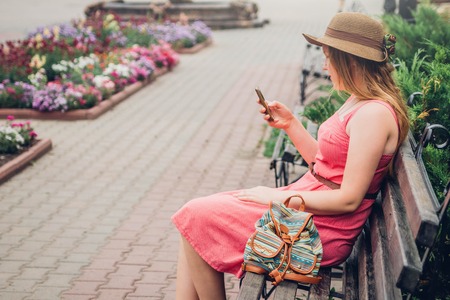Teenager girl uses her phone in the park sitting on benchの写真素材