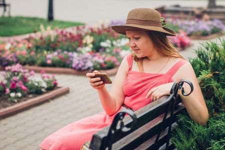 Teenager girl uses her phone in the park sitting on benchの写真素材