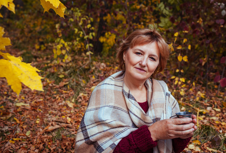 Happy middle-aged woman drinks tea in autumn forestの写真素材