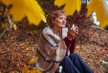 Happy middle-aged woman drinks tea in autumn forestの写真素材