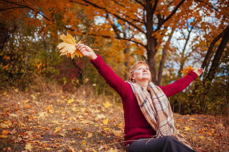 Middle-aged woman hthrowing leaves in autumn forest. Happy senior ladyの写真素材