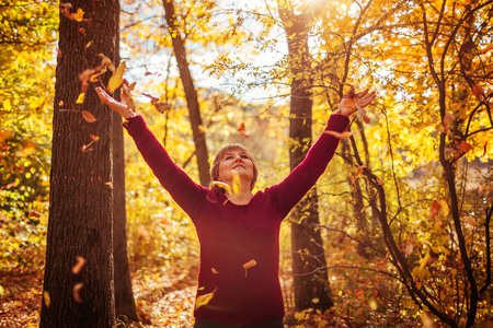 Middle-aged woman hthrowing leaves in autumn forestの写真素材