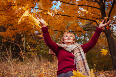 Middle-aged woman hthrowing leaves in autumn forest. Happy senior ladyの写真素材
