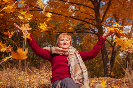 Middle-aged woman hthrowing leaves in autumn forest. Happy senior ladyの写真素材