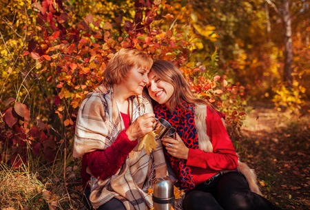 Middle-aged woman and her daughter having tea in autumn forestの写真素材
