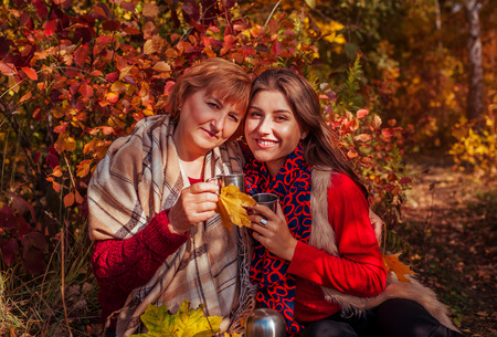 Middle-aged woman and her daughter having tea in autumn forestの写真素材