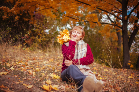 Middle-aged woman surrounded with yellow trees relaxes in autumn forest. Lady enjoying nature holding bouquet of leavesの写真素材