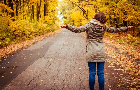 Young happy woman walks in autumn forest. Happy girl enjoying nature with raised handsの写真素材