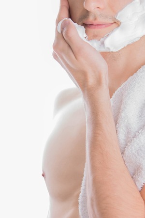 Young topless man with towel on shoulder applying shaving foam on white backgroundの写真素材