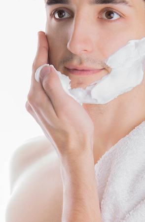 Young topless man with towel on shoulder applying shaving foam on white backgroundの写真素材