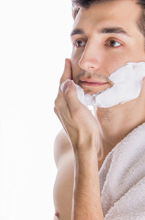 Young topless man with towel on shoulder applying shaving foam on white backgroundの写真素材