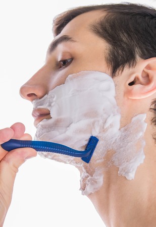 Young topless man with shaving foam applied shaving using razor on white backgroundの写真素材